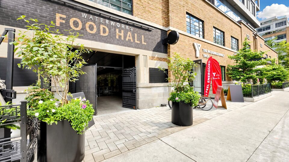 Entrance to the Waterworks Food Hall next to the YMCA, with black brick, gold lettering and planters