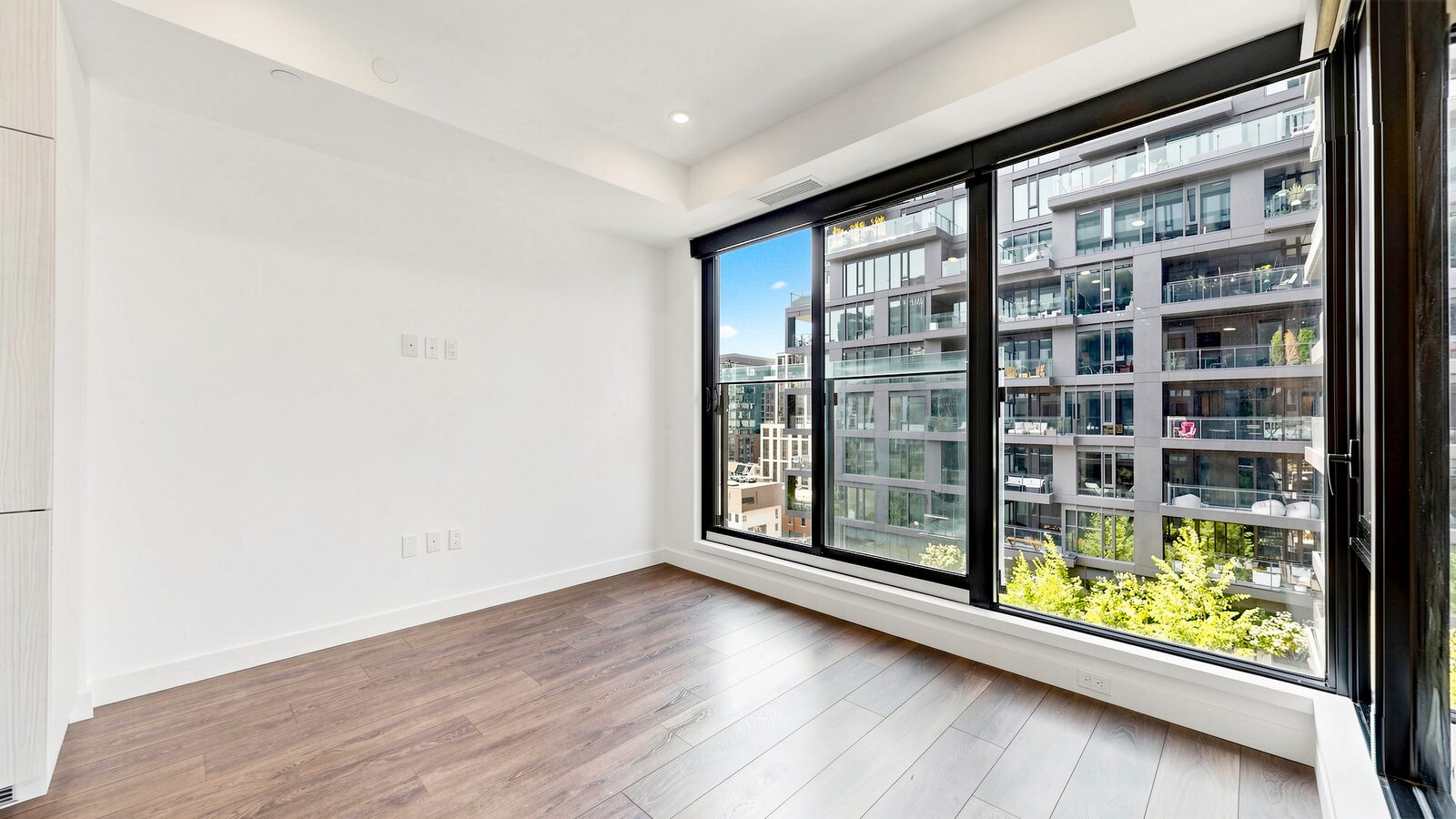 The same living room unfurnished, showing floor-to-ceiling windows and wide plank flooring
