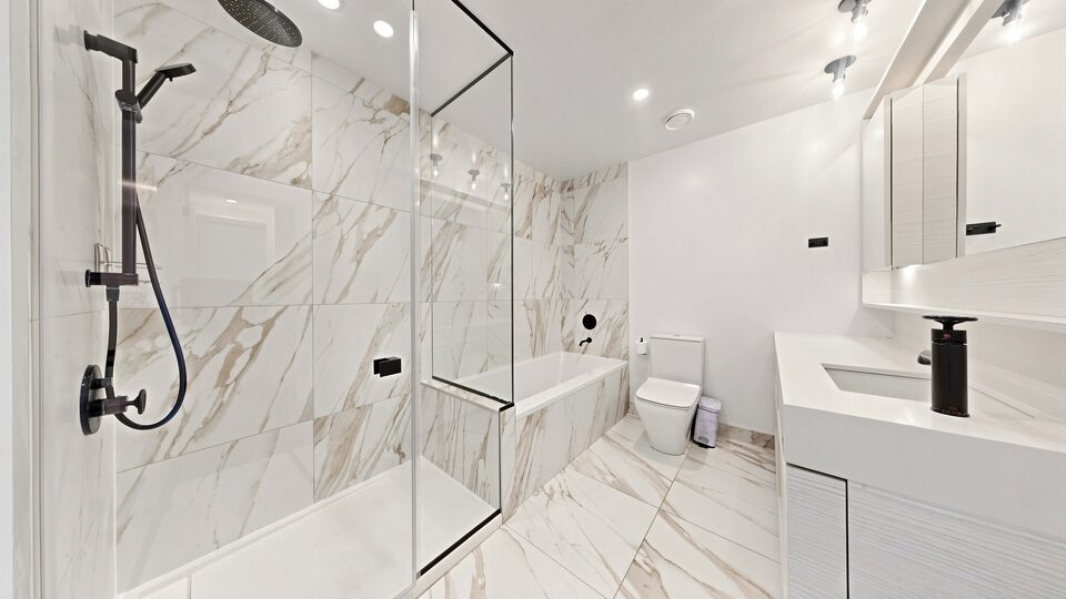 Primary ensuite in marble-look tile with a glass shower, deep tub and matte black fixtures