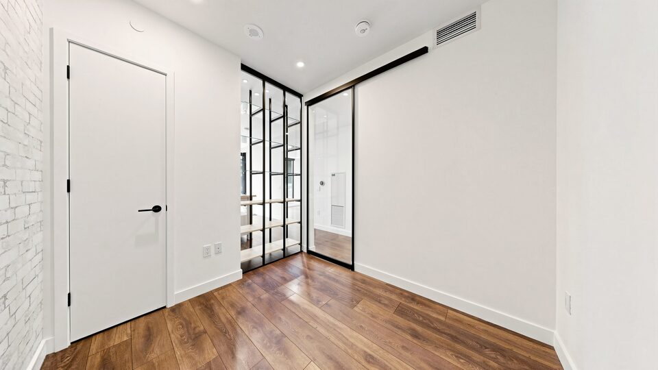 Second bedroom with whitewashed brick accent wall and glass-and-steel closet doors